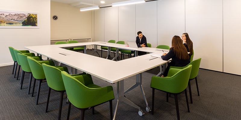 A man and two women are having a discussion around a large meeting room table